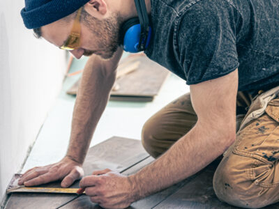 A male worker puts laminate flooring on the floor. Building contractor worker using hand held worm drive circular saw to cut boards on a new home constructiion project.
